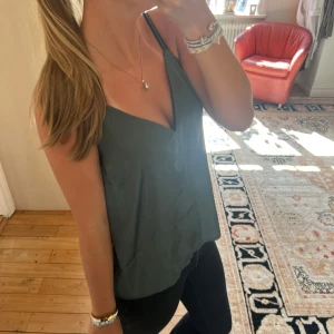 Mörkgrön linnetopp med v-ringning - Snygg mörkgrön linnetopp med djup v-ringning och tunna axelband. Toppen har en loose passform och är tillverkad i ett lent, silkesliknande material som ger en skön känsla mot huden. Perfekt att matcha med jeans eller kjol för en chill look.💛