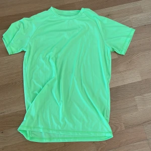 Neongrön t-shirt från Energetics - Fräsch neongrön t-shirt från Energetics i storlek 158/164. Tillverkad i mjukt och lätt polyester, perfekt för träning eller sport. Klassisk rund hals och korta ärmar, med en loose passform som ger skön rörelsefrihet. Snygg och enkel design utan mönster.