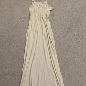 Ljus långklänning från Bubbleroom - Supersöt ljus långklänning från Bubbleroom med smala axelband och rynkade detaljer över bröstet och midjan. Klänningen är i mjukt material och har en flowy siluett som ger en chill och feminin vibe. Perfekt för varma dagar och somriga tillfällen.