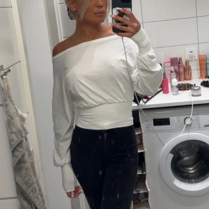 Vit offshoulder långärmad tröja - Säljer en vit långärmad tröja med offshoulder-design och bred midjeresår. Tröjan har en loose passform upptill och sitter tajt runt midjan, vilket ger en snygg siluett. Materialet känns mjukt och stretchigt, perfekt för dig som gillar trendiga och bekväma plagg.