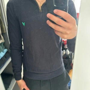 Mörkblå half zip tröja från Lyle & Scott - Mörkblå långärmad tröja från Lyle & Scott med half zip och ribbade muddar. Tröjan har en broderad grön logga på bröstet och är tillverkad i mjuk bomull. Perfekt för dig som gillar stilren och enkel design. Jag är 181cm och 75kg