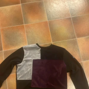 Blockmönstrad tröja från La Vichy - Säljer en unik långärmad tröja från La Vichy i storlek S. Tröjan har blockmönster i svart, grått och mörklila med sammetsdetaljer på framsidan. Rund hals och patch med logga på ena ärmen. Perfekt för dig som gillar statement-plagg och coola färgkombinationer.