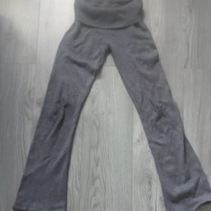 Grå stickade byxor från Gina Tricot - Mysiga grå stickade byxor från Gina Tricot med bred ribbad midja och utsvängda ben. Perfekta för chill dagar hemma eller när du vill vara extra bekväm. Materialet är mjukt och stretchigt, vilket gör dem riktigt sköna att ha på sig.