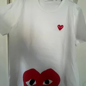 Vit Comme des Garçons Play t-shirt - Säljer en vit t-shirt från Comme des Garçons Play storlek M men sitter mer som S.med ikoniskt rött hjärta med ögon på bröstet och ett stort hjärta med ögon tryckt längst ner. T-shirten har rund hals och korta ärmar, tillverkad i mjuk bomull.