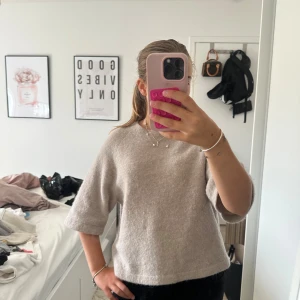 Beige stickad tröja med trekvartsärm - Mysig beige stickad tröja med rund hals och trekvartsärmar. Tröjan har en loose passform och är perfekt för dig som gillar en enkel och chill stil. Materialet är mjukt och fluffigt, vilket gör den skön att bära under kyliga dagar.