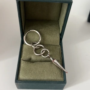 Silvrigt örhänge med kedja och spike - Tappat färg men fortfarande väldigt vackert! Coolt örhänge i silverfärgad metall med chunky ringar och en spetsig spike-hängare. Designen är edgy och sticker ut, perfekt för dig som gillar statement-smycken. Liknar Maria Nilsdotter men är ej det!
