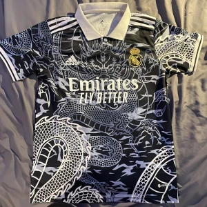Real Madrid fotbollströja - Real Madrid special edition, storlek S men passar M, lite så i axlarna isåfall. Har ett drakmotiv. Använd ett par gånger men i gott skick. Dock har lite print försvunnit (se bild 2)