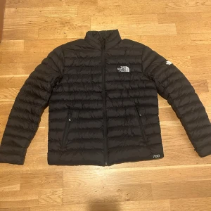 Svart dunjacka från The North Face - Säljer en svart dunjacka från The North Face med diskret logga på bröstet och ärmen. Jackan har quiltad design, dragkedja framtill och två fickor med dragkedja. Perfekt för kalla dagar och enkel att matcha med allt. Klassisk och stilren look. Kan bli till två olika modeller 