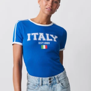 Blå Italy t-shirt - Snygg blå t-shirt med vit kant vid hals och ärmslut, samt vita ränder på axlarna. Tryck med 'ITALY EST:1989' och italienska flaggan på bröstet. Perfekt för dig som gillar sportig och retro stil.