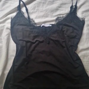 Svart linnetopp med spets från Coster - Svart linnetopp från Coster Copenhagen med tunna axelband och snygga spetsdetaljer längs v-ringningen. Oanvänd.💗
