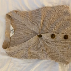 Beige ribbad kofta med knappar - Säljer en beige ribbad kofta från H&M med snygga bruna knappar framtill. Koftan har lång ärm och är gjord i ett mjukt, tunt stickat material som känns skönt mot huden. Perfekt att slänga på sig när det är lite kyligt ute.