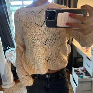Beige stickad tröja med hålmönster - Säljer en beige stickad tröja med snyggt hålmönster och loose passform. Tröjan har långärmade ärmar och är lite croppad i modellen, perfekt att styla med höga jeans. Mjuk och skön, passar dig som gillar en chill och trendig look.