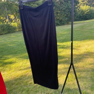 Svart långkjol från Pretty Little Thing - Svart långkjol från Pretty Little Thing i enkel och stilren design. Kjolen har slim passform och är gjord i mjukt, stretchigt material som sitter bekvämt. Perfekt att matcha med crop tops eller hoodies för en chill vibe.