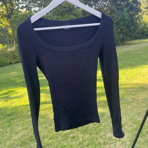 Svart långärmad topp Gina Tricot - En svart, ribbad långärmad topp från Gina Tricot med rundad, bred urringning. Tight passform och stretchigt material som sitter snyggt på kroppen. Perfekt att styla med jeans eller kjol för en clean look.
