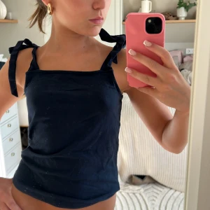 Mörkblå linnetopp med knytaxlar - Supersöt mörkblå linnetopp med knytbara axelband och rak halsringning. Perfekt för varma dagar och enkel att styla med jeans eller kjol. Tunn och skön känsla, passar dig som gillar en enkel men trendig look.