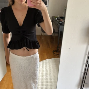 Svart volangtopp från Bik Bok - Säljer en svart topp från Bik Bok med volang nertill och puffärmar. Toppen har v-ringning och har en knytning framtill. Perfekt till sommaren!