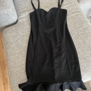 Svart volangklänning från BikBok - Säljer en svart klänning från BikBok med smala axelband och volangdetalj nertill. Klänningen har en figurnära passform och dragkedja i ryggen. Perfekt för dig som vill ha en stilren och enkel look.