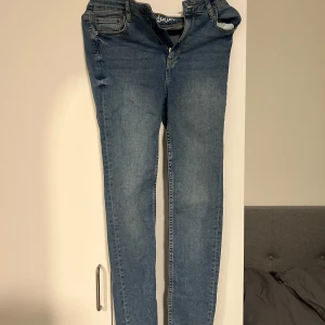 Blå skinny jeans med dragkedja - Säljer ett par klassiska blå skinny jeans med dragkedja och knapp framtill. Jeansen har fem fickor och en smal passform som sitter tight längs benen. Perfekta till vardags och lätta att matcha med olika toppar. Oanvänd 