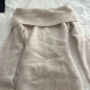 Beige offshoulder stickad tröja från Gina Tricot - Supermjuk och mysig beige stickad tröja från Gina Tricot med bred offshoulder-krage. Aldrig använd då den va för liten men otroligt gosig, fin och har ribbade detaljer vid krage och nederkant. Nypris: 250kr