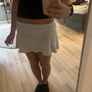 Ljusgrå kort kjol med volang - Supersöt ljusgrå kort kjol. Kjolen har en mjuk och stretchig passform som sitter bekvämt i midjan. Perfekt för dig som gillar en enkel men ändå trendig stil.