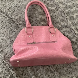 Rosa handväska  - Säljer en rosa handväska med krokodil mönster och silverfärgade detaljer. Väskan har dubbla handtag, dragkedja upptill och ett ytterfack med dragkedja. Insidan är svart med innerfack. 💕🌸