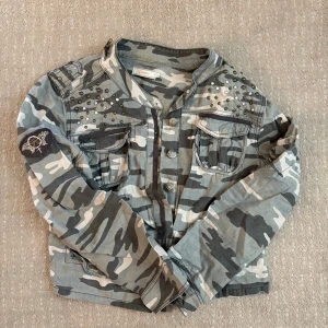 Camouflage jacka med nitar från Chasin - Säljer en grå och grön camouflage jacka från Chasin med coola nitar på axlarna och två bröstfickor med lock. Supersnygg men kommer tyvärr inte till användning längre