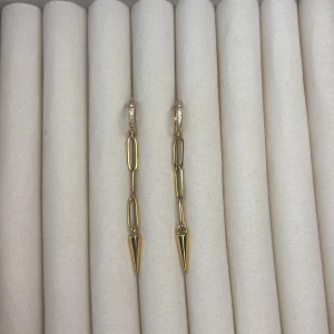 Guldiga örhängen med kedjor och spetsdetalj - Säljer ett par trendiga guldiga örhängen med avlånga kedjelänkar och spetsiga hängen. Örhängena har små gnistrande stenar på ringen upptill för extra bling. Perfekta för dig som gillar statement-smycken!