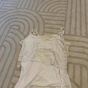 Vit linnetopp med spetsdetaljer - Säljer en söt vit linnetopp med tunna axelband och vackra spetsdetaljer framtill. Perfekt för varma dagar eller som ett lager under en kofta. Toppen har en avslappnad passform och fina broderade mönster på bröstet.
