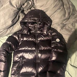 Moncler Maya - Säljer en svart pufferjacka från Moncler med huva och dragkedja. Jackan har två fickor med dragkedja och klassisk Moncler-logga på ärmen. Perfekt för kyliga dagar och riktigt snygg streetstil. Skick: 9/10. Size S. PENGARNA KOMMER INTE MED!!!!