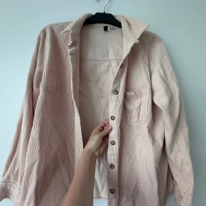 Ljusrosa manchester-skjorta från Divided - Säljer en ljusrosa manchester-skjorta från Divided. Skjortan har långa ärmar, klassisk krage, bröstficka och knäppning framtill. Perfekt att styla lager på lager eller bära som den är.