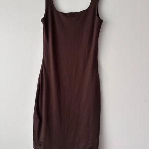 Brun ärmlös klänning från amisu  - Säljer en enkel och stilren brun ärmlös klänning från  amisu . Klänningen har en rak passform och är tillverkad i ett mjukt material som känns skönt mot huden. Perfekt för varma dagar eller att styla med en kavaj.