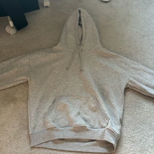 Grå hoodie från BikBok - Säljer en enkel och stilren grå hoodie från BikBok i storlek XS. Tröjan har huva med dragsko och en stor magficka framtill. Perfekt för en avslappnad look och passar året runt.