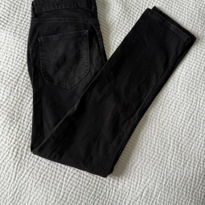 Svarta jeansbyxor från Lee - Säljer ett par svarta jeansbyxor från Lee i modellen Washed Black. Byxorna har klassisk femficksdesign, normal passform och raka ben. Tillverkade i bomull med lite elastan för extra komfort. Perfekta till vardags och enkla att matcha.