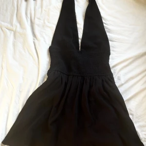 Svart halterneck & openback klänning  - Säljer en svart klänning med omlott och halterneck. Klänningen har en tight överdel med smock och en utställd kjol. Knappt använd 