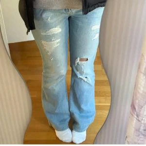 Ljusblå bootcut jeans - Säljer ett par ljusblå bootcut jeans med slitningar på framsidan. Jeansen har en låg midja och klassiska femficksdetaljer.