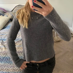 Grå stickad tröja från Zara - Mysig grå stickad tröja från Zara med croppad passform. Tröjan har rund halsringning och långa ärmar med ribbade muddar. Super mjuk i cashmere och ull super enkel att matcha till olika outfits!