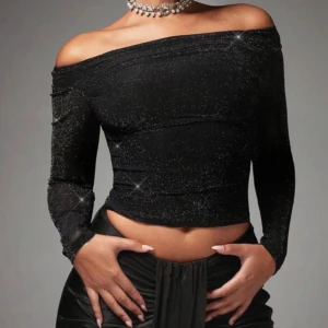 Svart glittrig offshoulder topp - Säljer en svart glittrig topp med offshoulder-design och långa ärmar. Toppen är tight och har en snygg croppad passform, perfekt för att sticka ut på festen. Sitter som en S