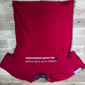 Röd t-shirt från Sail Racing - Röd t-shirt från Sail Racing med tryck 'SAIL RACING INTERNATIONAL' och japanska tecken på framsidan. Har en patch med texten 'JPN 77 EXTREME SAILING' på ärmen. Rund halsringning och normal passform.