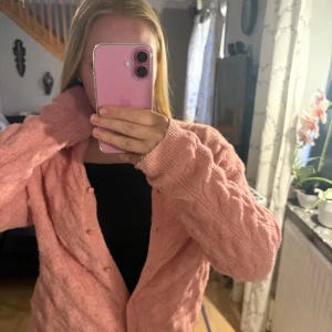 Rosa stickad kofta med knappar - Mysig rosa stickad kofta med kabelstickat mönster och rund hals. Koftan har långa ärmar och stängs med matchande rosa knappar framtill. Perfekt för lager-på-lager och en söt detalj till din outfit.( pris går alltid att diskutera)