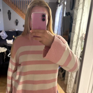 Rosa och vit randig stickad tröja - Säljer en söt stickad tröja med breda rosa och vita ränder. Tröjan har lång ärm, rund hals och ribbade muddar vid ärmslut och nederkant. Perfekt för en mysig och avslappnad stil.( pris går att diskutera)