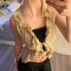 Beige volangväst/ blus från Vila - Säljer en beige väst/ blus från Vila med volangdetaljer och spets längs kanterna. Västen har knytband i fram och i bak så att man kan justera hur tajt/ löst man vill att den ska sitta. tillverkad i ett tunt, lätt material. Den är i strl L men jag är xs/s och kan justera den så att den passar mig också. Mycket bra skick, inga defekter. Köpt secondhand sen innan! Pris går alltid att diskutera. Skriv om funderingar osv❣️