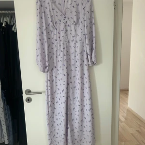 Ljuslila långklänning med blommigt mönster - Säljer en söt långklänning i ljuslila med små blommor. Klänningen har v-ringning och långa ärmar, perfekt för vår och sommar. Den har en feminin och flowy passform som känns både romantisk och trendig.