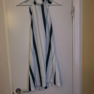 Randig ärmlös klänning - Säljer en snygg ärmlös klänning med höghalsad design och vertikala ränder i vitt, blått, grönt och svart. Klänningen har en luftig passform och är perfekt för varma dagar.