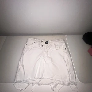 Vit jeanskjol med fransig kant - Säljer en vit jeanskjol från 151 med rå, fransig nederkant och klassiska fickor både fram och bak. Kjolen har knapp- och dragkedjestängning framtill och är perfekt för en trendig och avslappnad look.
