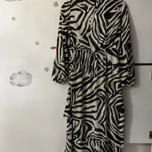 Zebramönstrad långklänning från LC Waikiki - Säljer en långklänning från LC Waikiki med svartvitt zebramönster. Klänningen har långa ärmar, markerad midja och volangdetalj nertill. Perfekt för dig som gillar djurmönster och vill sticka ut.