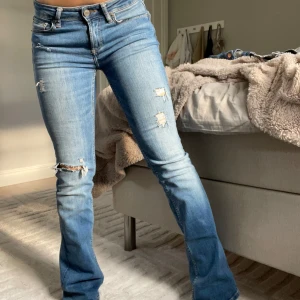 Lågmidjade bootcut jeans - Säljer ett par blå bootcut jeans med slitningar för en coolare look. Jeansen har låg midja och är i ett mjukt denimtyg. Mycket bra skick! Hör av er vid frågor!💕