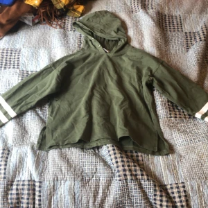 Grön hoodie med huva - Säljer en grön hoodie med huva och vita ränder på ärmarna. Jackan har en avslappnad passform och är perfekt för en chill vardagsstil. Materialet känns mjukt och bekvämt, och modellen har långa ärmar.