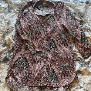 Mönstrad skjorta i svart, rött och vitt - Säljer en skjorta med unikt grafiskt mönster i svart, rött och vitt. Skjortan har lång ärm, klassisk krage och knäppning framtill. Perfekt för dig som vill sticka ut med en cool och färgstark look.