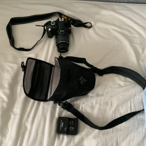 Nikon D60 - Säljer en svart axelväska perfekt för systemkamera och tillbehör. Väskan har justerbar axelrem och flera fack för att organisera kamerautrustning. Enkel och stilren design som passar till de flesta kameramodeller.