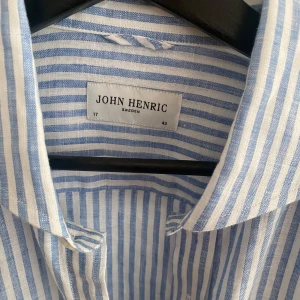 Blåvit randig linneskjorta från John Henric - Säljer en snygg blåvit randig skjorta från John Henric som jag aldrig har använt. Skjortan har klassisk krage och knäppning framtill. Perfekt för en fräsch och stilren look till sommaren. Storlek 43 alltså mellan L och XL